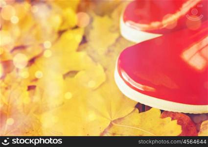 footwear, autumn and season concept - close up of red rubber boots on fallen yellow autumn leaves