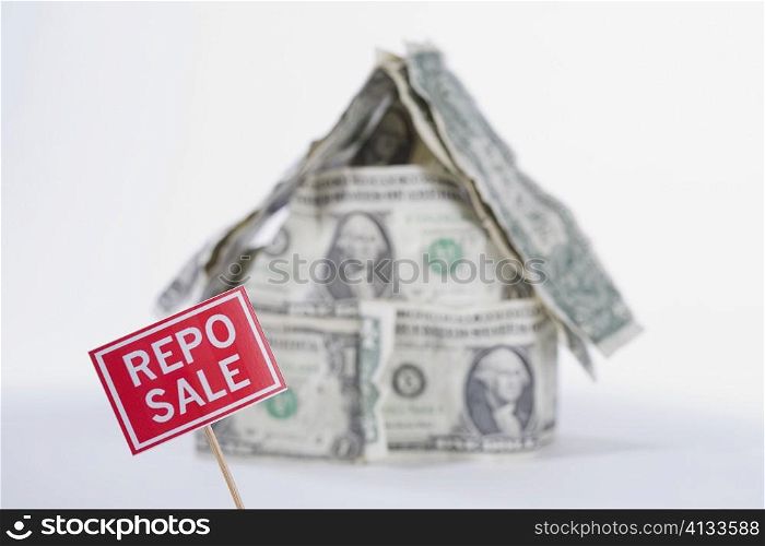 For Sale board in front of a miniature house made up of US dollar bills