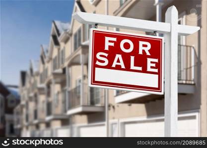 For Sale Real Estate Sign In Front of a Row of Apartment Condominiums Balconies and Garage Doors.