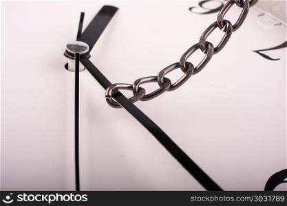 Forcing the time to change. chain tied to minute hand of a clock and pulled on a white background