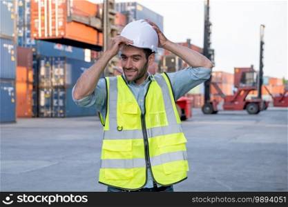 Foreman engineer or cargo container worker hold hardhat and stand in front of cranes and stack of shipping. Logistic shipyard management system and safety concept.