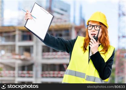 foreman with a walkie-talkie in a vest and a yellow helmet against the background of the building under construction