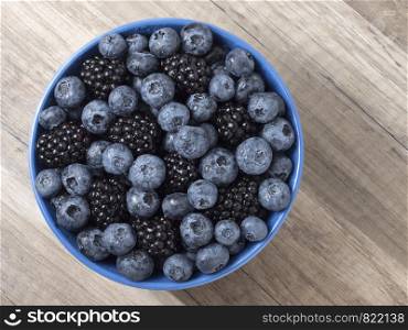 Forest berries (blueberry,bramble) in a ceramic blue bowl. Top view. Space for text.