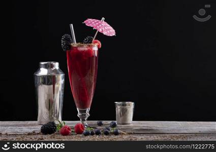 forest fruit cocktail in a glass on a wooden base decorated with blackberries and a shaker