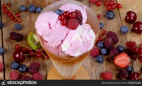 Forest fruits ice cream in cup rotating on wooden table full of summer berries fruits.