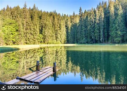 Forest lake in the mountains with blue water, wooden bridge, morning light and shining sun. Forest lake in the mountains