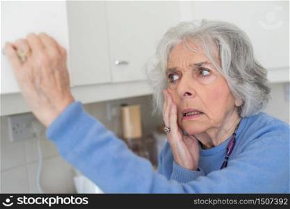 Forgetful Senior Woman With Dementia Looking In Cupboard