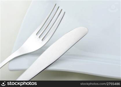 Fork and a knife laying on a plate. A photo close up