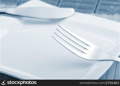 Fork and a knife laying on a plate. A photo close up. Blue tone