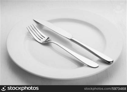 Fork and knife lying on the empty white plate. Cutlery on a plate