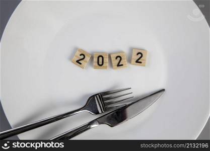 Fork and knife on a white empty plate with 2022 text top view, New year diet, healthy eating concept background eating. Fork and knife on a white empty plate with 2022 text top view, New year diet, healthy eating concept background