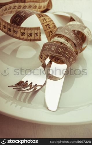 Fork and knife with meter on the empty white plate, diet concept