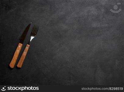 Fork and knife with wooden handle on black background, top view