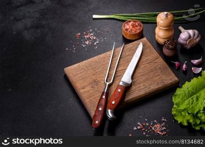 Fork, knife, spices and herbs, cutting board on a dark concrete background. Cooking at home. Fork, knife, spices and herbs, cutting board on a dark concrete background