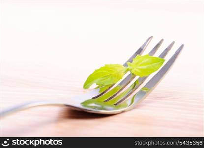 Fork on wooden table with green leaf of basil. Close up, selective focus