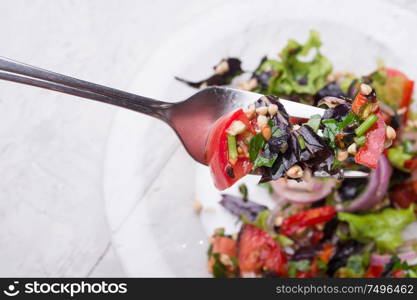 fork with vegetarian fresh salad with vegetables, herbs and sprouts of buckwheat. beautiful served in transporant bowl at white table. healthy raw eating food. close up
