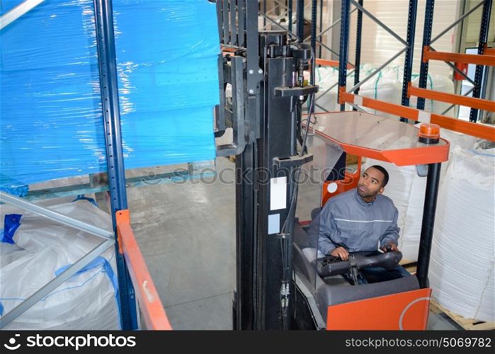 Forklift driver stacking pallet high in racking
