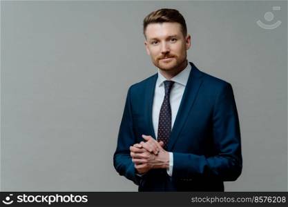 Formal style. Serious bearded male entrepreneur keeps hands together wears formal clothes dressed in office attire poses against grey background with copy space for your promotional content.