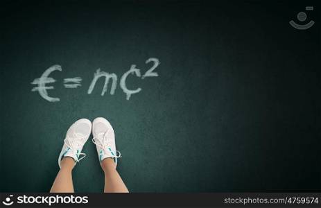 Formula in physics. Top view of girl in sport shoes standing on blackboard