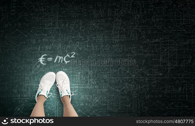Formula in physics. Top view of girl in sport shoes standing on blackboard