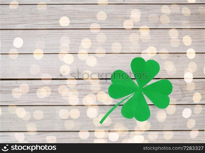 fortune, luck and st patricks day concept - green paper four-leaf clover over grey wooden boards background and festive lights. green paper four-leaf clover on wooden background