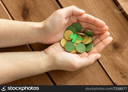 fortune, luck and st patricks day concept - hands holding golden coins and shamrock leaf on wooden background. hands with golden coins and shamrock leaf