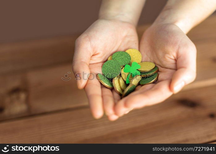 fortune, luck and st patricks day concept - hands holding golden coins and shamrock leaf on wooden background. hands with golden coins and shamrock leaf