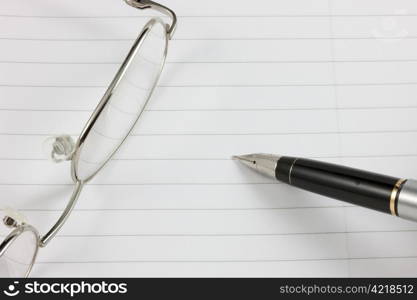 Fountain pen and glasses on a lined notepad with copy space