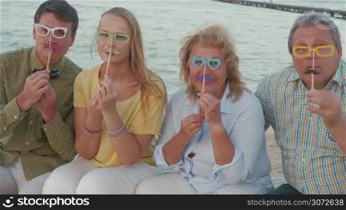 Four adult people trying on false paper glasses and mousctache.