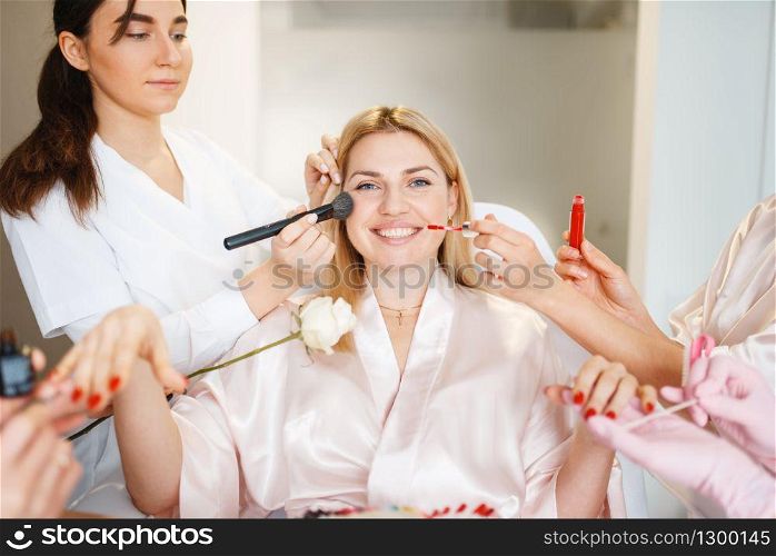Four beauticians and one female customer, makeup, pedicure and manicure procedure in beauty salon. Professional service, toenail and fingernail care in spa studio