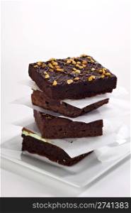 Four beautifully stacked gourmet brownies stacked on a white plate with parchment paper between each brownie.