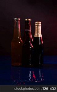 four beer bottles on a black and purple background with reflections on a shiny blue surface.. four beer bottles on a black and purple background with reflections on a shiny blue surface