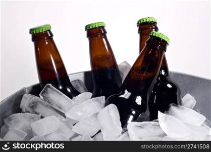 Four brown beer bottles on ice with bright green caps shot on white.