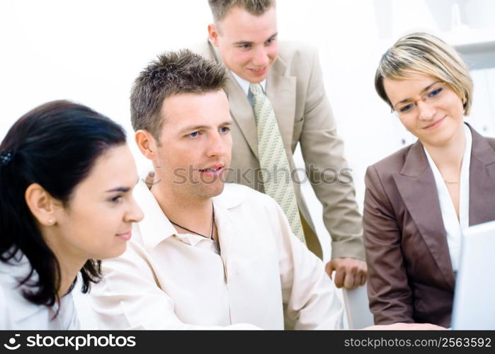 Four business colleagues working together on laptop computer in office, looking at screen, smiling.