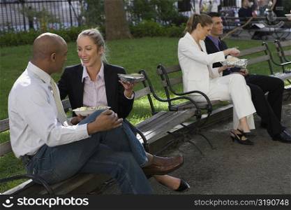 Four business executives having food on park benches