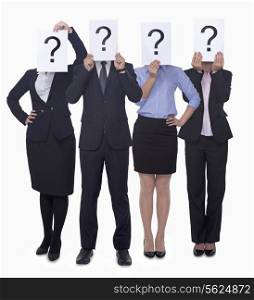 Four business people holding up paper with question mark, obscured face, studio shot