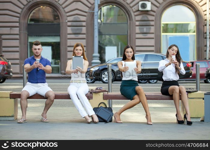 Four business people sitting on a bench in the summer city