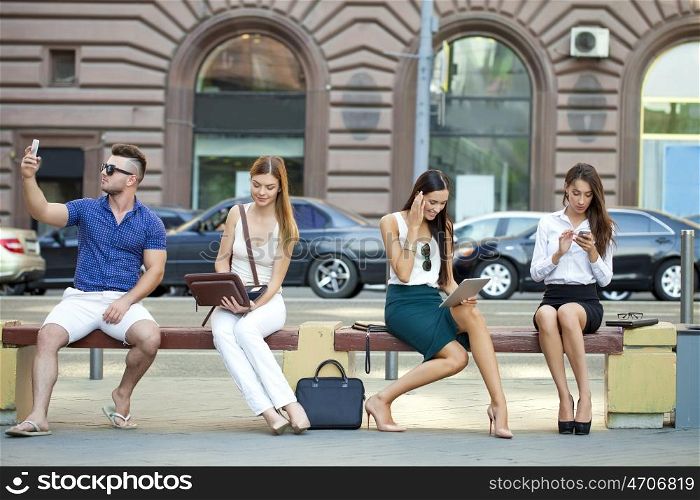 Four business people sitting on a bench in the summer city