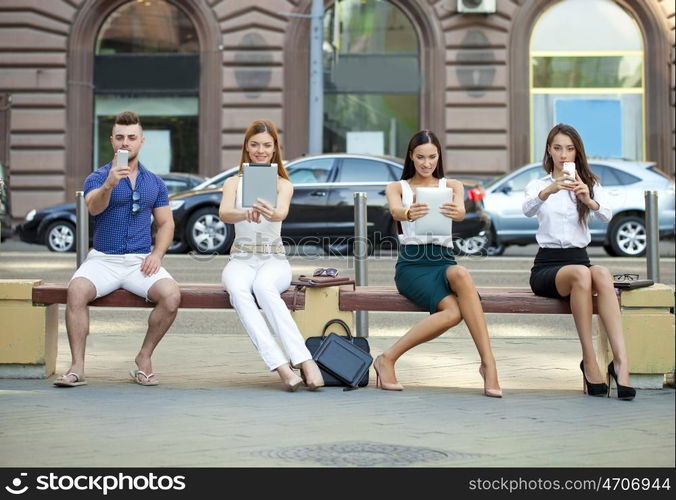 Four business people sitting on a bench in the summer city