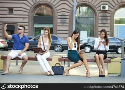 Four business people sitting on a bench in the summer city