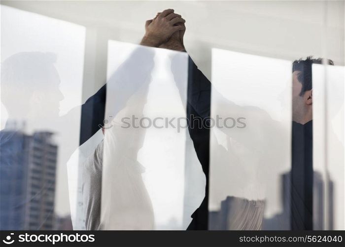 Four business people standing and cheering with hands together on the other side of a glass wall