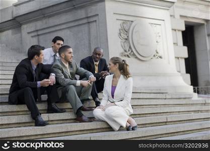 Four businessmen and a businesswoman sitting on steps and discussing