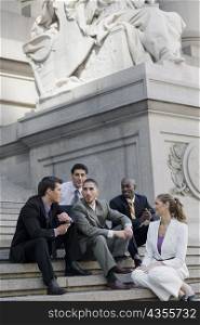 Four businessmen and a businesswoman sitting on steps and discussing