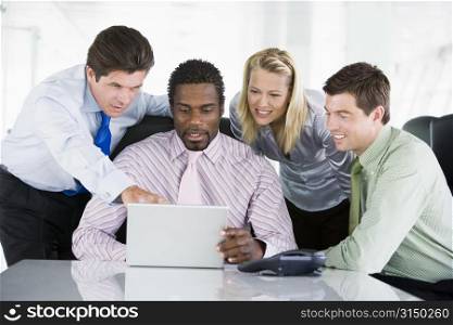 Four businesspeople in a boardroom pointing at laptop and smiling