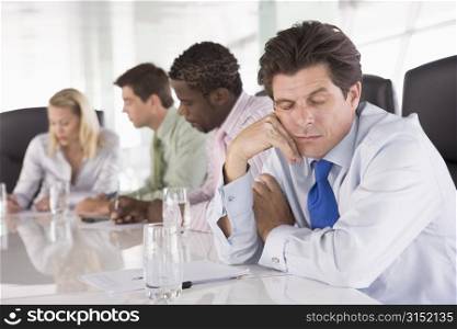 Four businesspeople in boardroom with one businessman sleeping