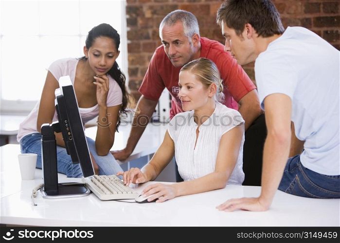 Four businesspeople in office space looking at computer smiling