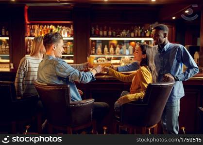 Four cheerful friends drinks beer at the counter in bar. Group of people relax in pub, night lifestyle, friendship, event celebration. Four cheerful friends drinks beer in bar