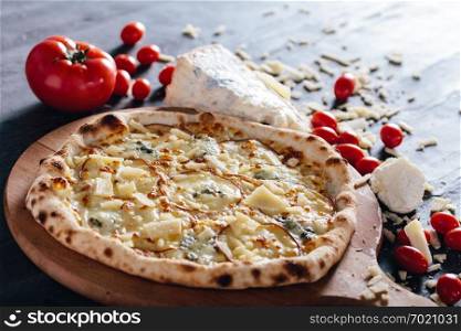 Four cheese pizza on wooden board. Tomatoes, blue cheese, parmesan and mozzarella in the background. Popular traditional food.. Four cheese pizza on wooden board.