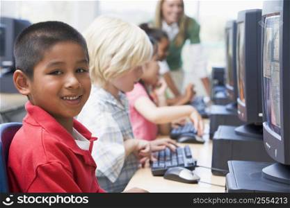 Four children at computer terminals with teacher in background (depth of field/high key)
