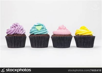 Four chocolate cup cakes with frosting or icing, pink, purple, yellow and blue with green leaf, photographed on a white background